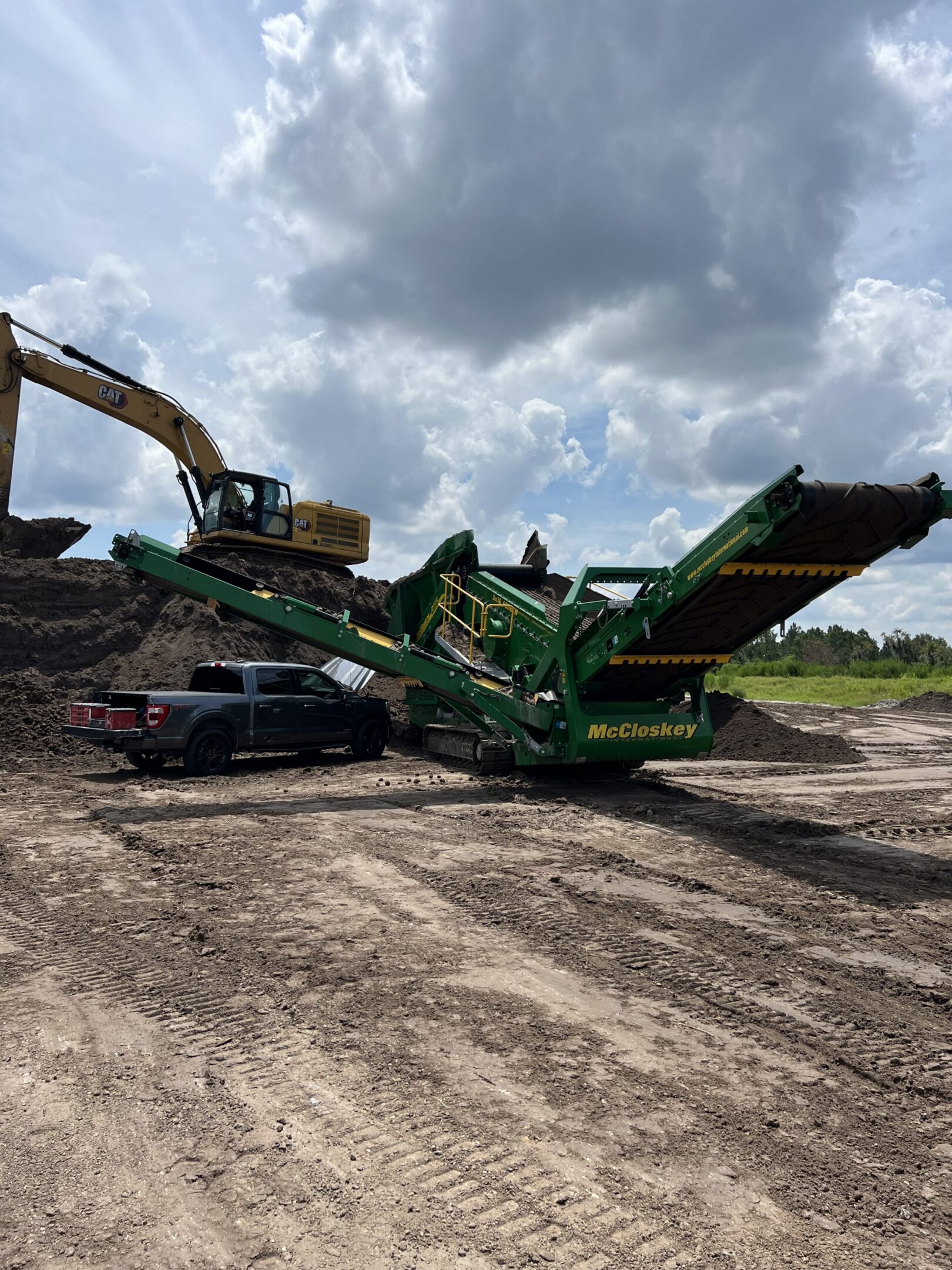 Green McCloskey screener with excavator and pickup